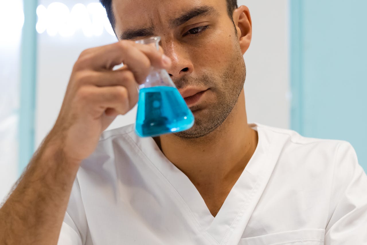 Scientist in lab coat examining blue liquid in flask, focused on experiment.